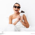 picture of a happy woman in a towel wearing sunglasses eating chocolate